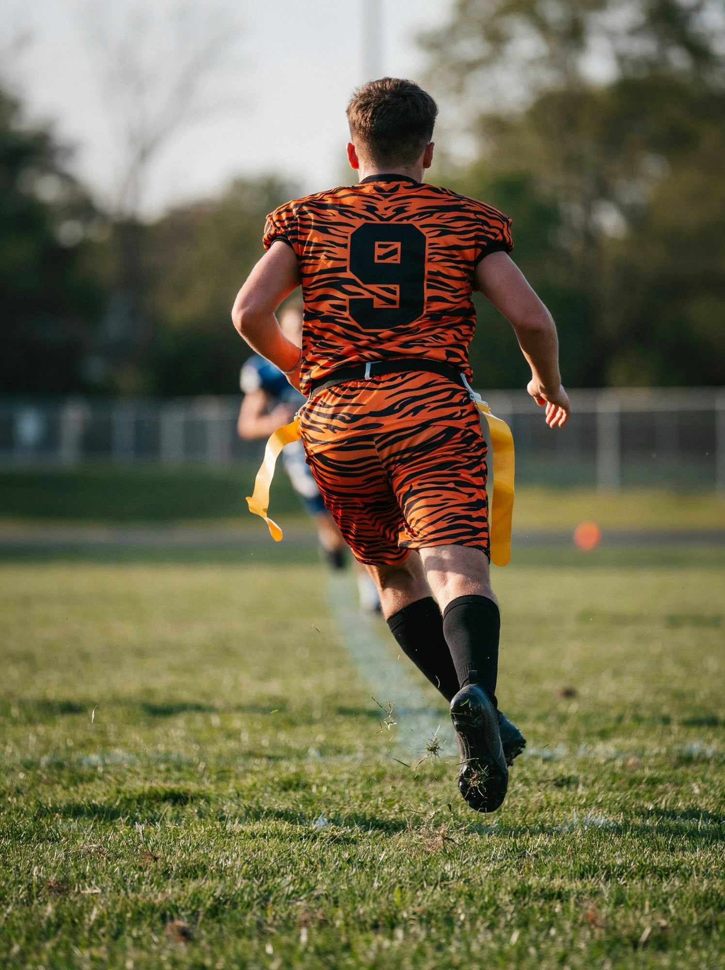 A flag football player sprinting away in a custom orange and black tiger stripe jersey with number 9