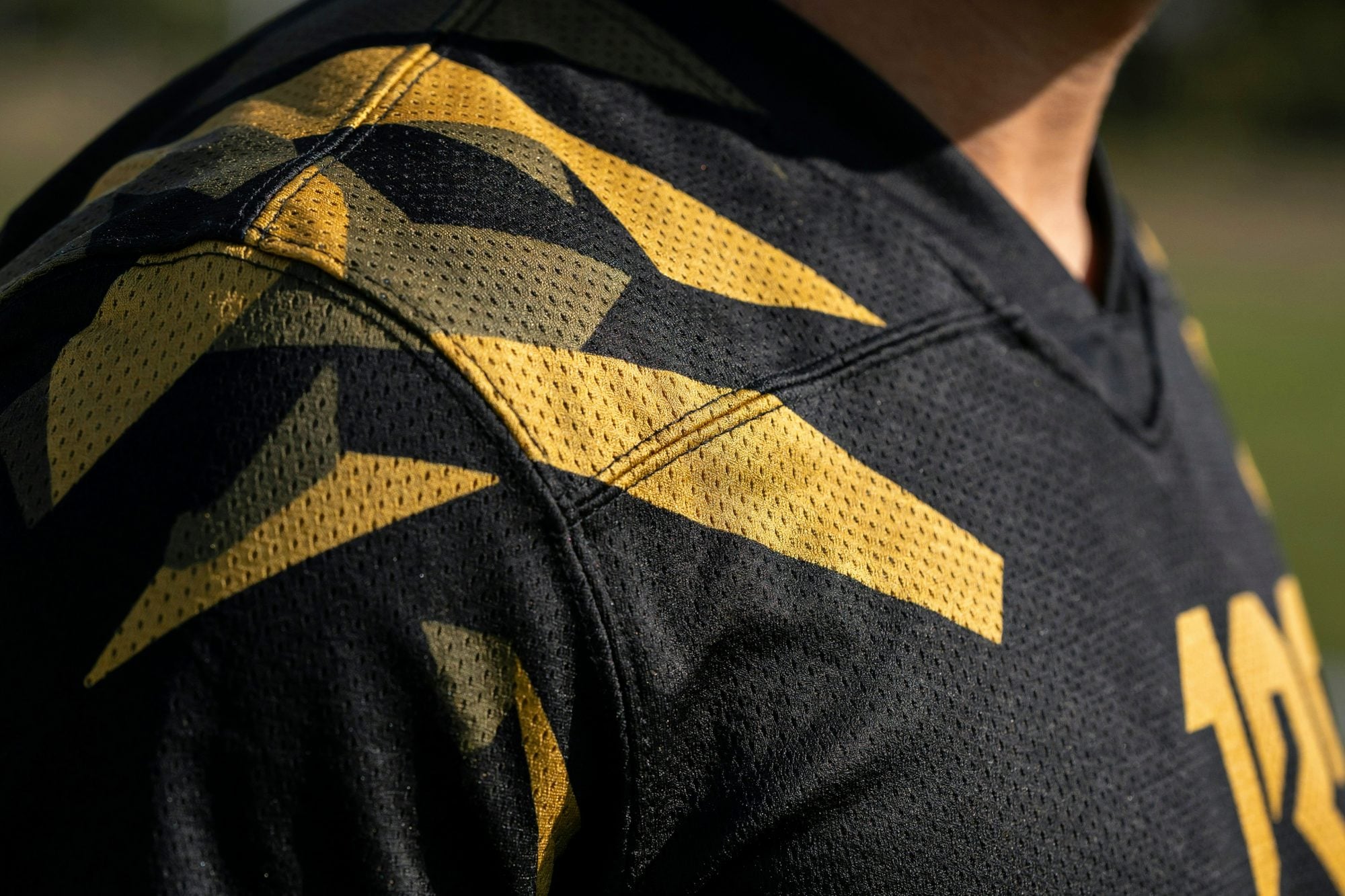 Close-up of black and gold sublimated mesh fabric with the edge of a gold number 12