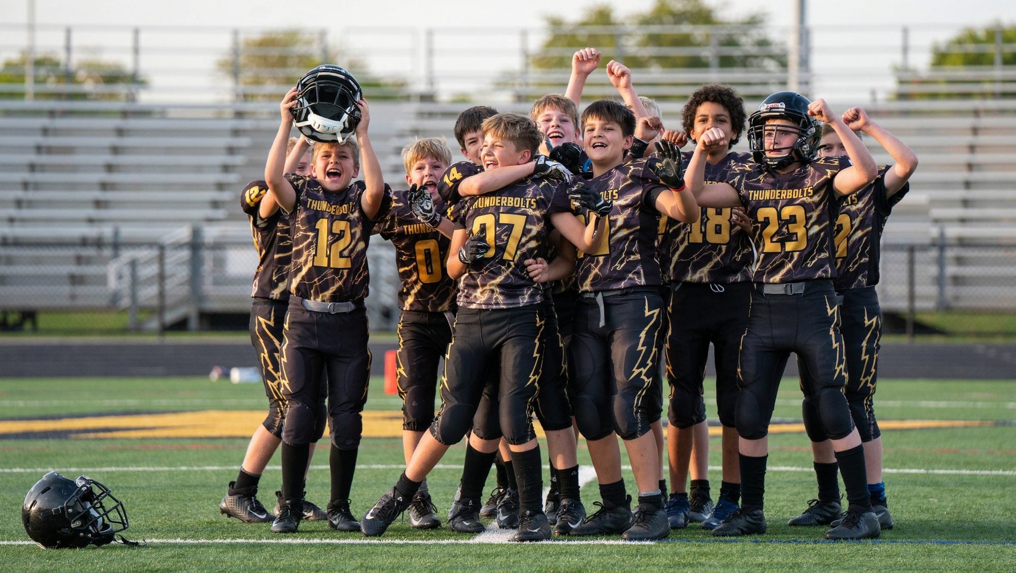 A youth tackle football team celebrating together on the field in custom black and gold THUNDERBOLTS uniforms