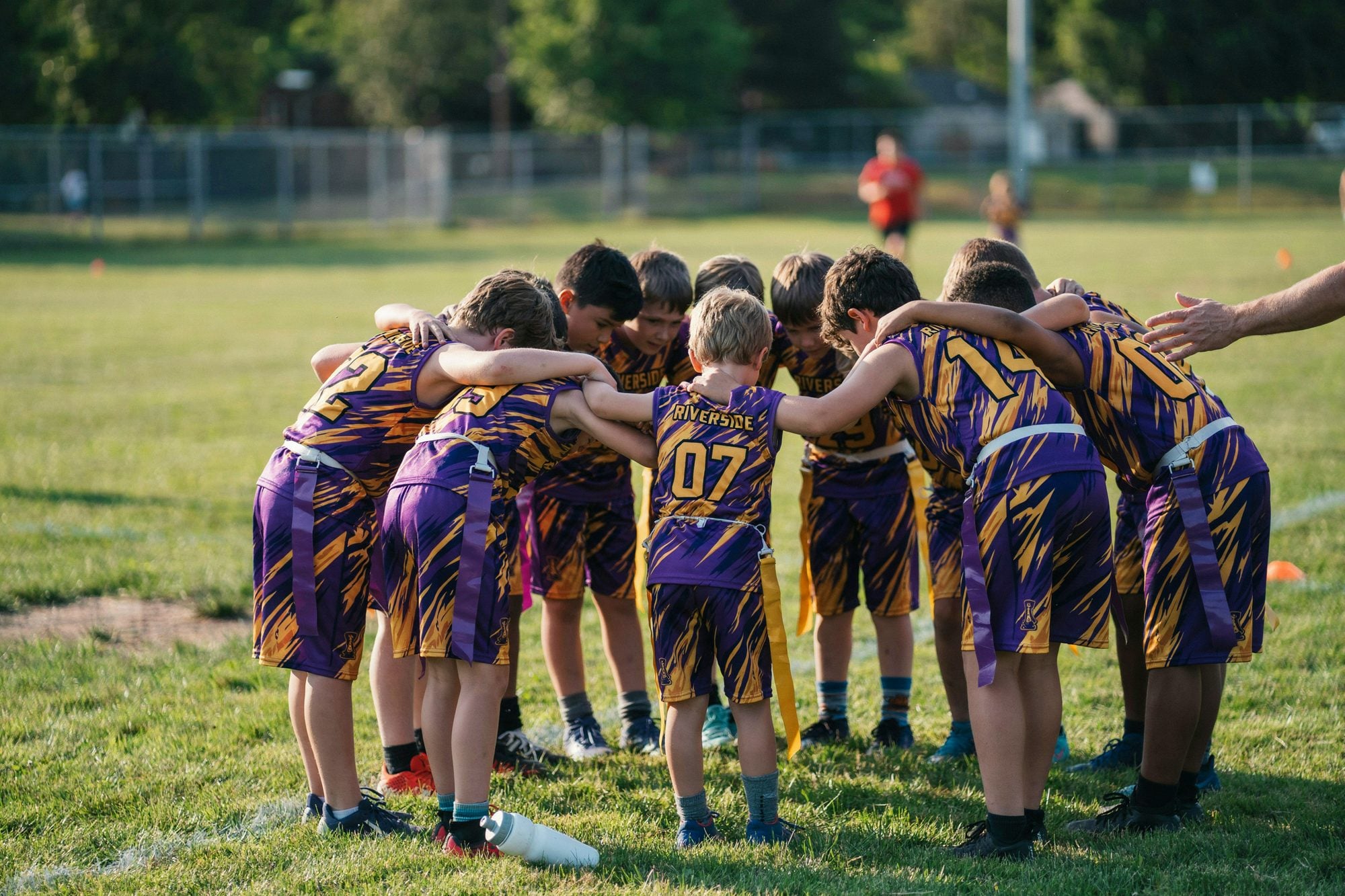 A youth flag football team huddling in custom purple and gold uniforms with flag belts