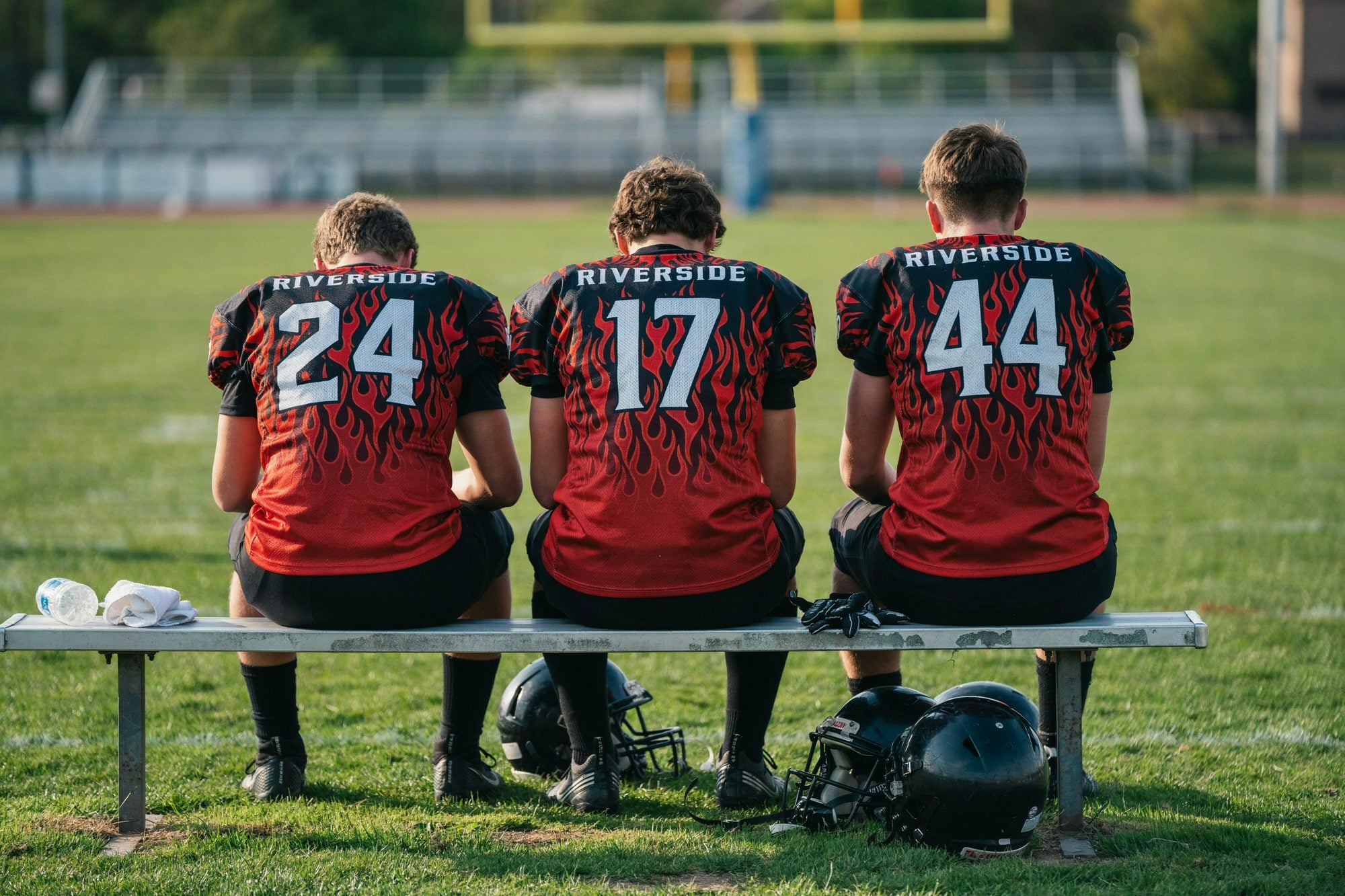 Players on the sideline bench seen from behind in custom red and black flame jerseys with numbers 24, 17 and 44
